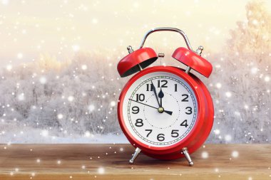 Saat on iki yönünde kış manzarası ve kar yağışı bulanık bir arka plan üzerinde kırmızı retro çalar saat. Gece yarısı, öğle vakti. Yeni yıl hakkında dakika.