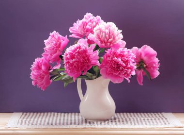 peonies mor bir arka plan üzerinde beyaz bir sürahi içinde yemyeşil buket. Bahçe çiçek.