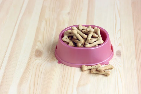 Comida para perros, galletas en forma de hueso en un tazón de plástico rosa, vista superior . — Foto de Stock