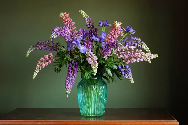 Mooi boeket van lupine en irissen in een glazen vaas. — Stockfoto