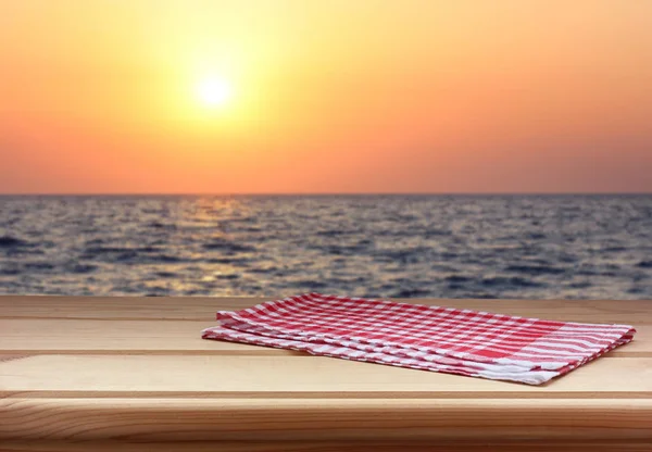 Άδειο τραπέζι με μια κόκκινη πετσέτα κατά το ηλιοβασίλεμα στη θάλασσα. — Φωτογραφία Αρχείου