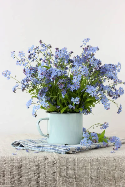 テーブルの上にテーブルクロスの上のエナメルマグカップにブルーの忘れられない私ではありません 庭の花と共に生きる — ストック写真