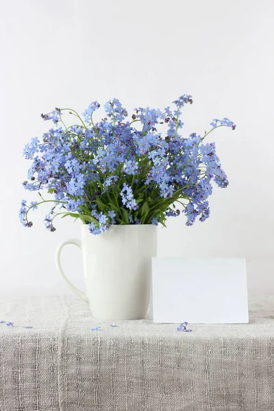 白いマグカップの中の青の忘れられない私の花束と光の背景に空の紙のカード モックアップ テンプレート — ストック写真
