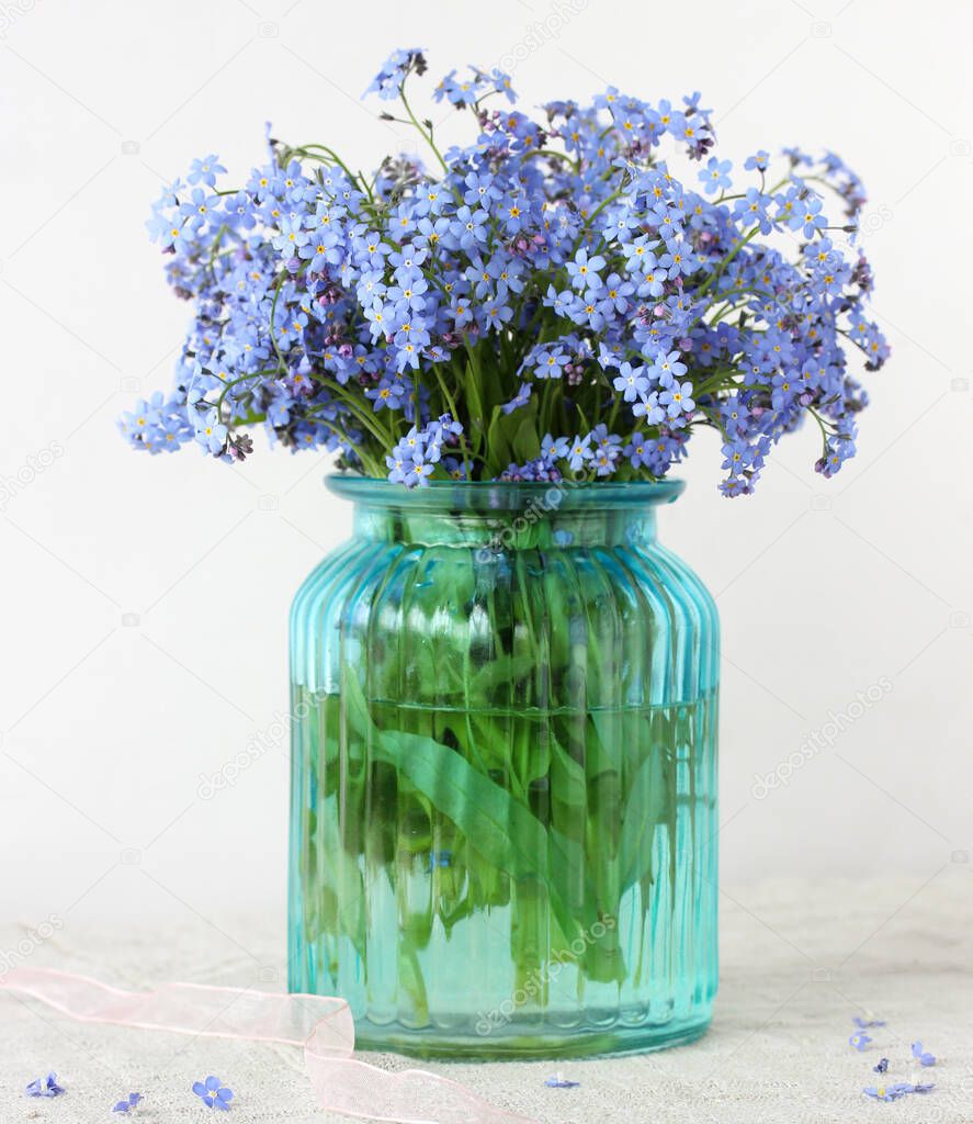 blue forget-me-nots in a glass vase on a table with a light tablecloth. still life with garden flowers.
