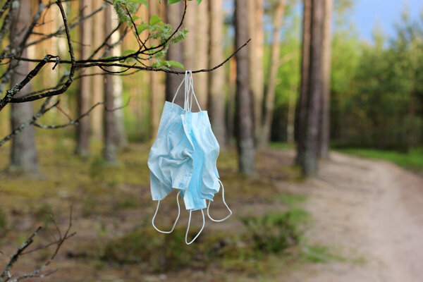 used medical masks hang in a forest on a tree. pollution of nature.