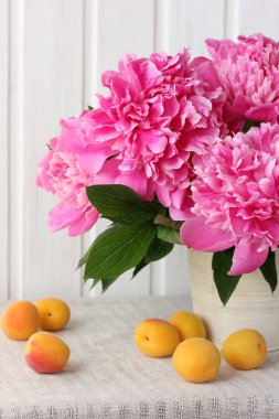 Pembe şakayıklar ve kayısılar. Masanın üzerinde bir buket çiçek ve meyve..