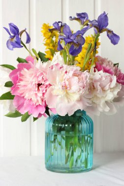 Açık arkaplanda bir buket pembe şakayık ve süsen çiçeği. Bahçe çiçekleri cam vazoda.