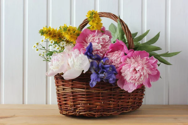 一束粉红色的牡丹和虹膜在一个篮子里 放在一个背景浅的桌子上 花园花 — 图库照片