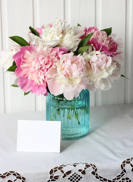 モックアップシーン作成者 ガラスの花瓶にピンクの牡丹レースのテーブルクロステーブルに空のカード 庭の花の花束 — ストック写真