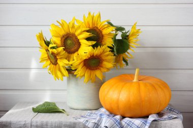 Ayçiçeği buketi ve arka planda masanın üzerinde bir balkabağı. Bahçe çiçekleri ve sebzeler, yaz durgun hayatı.