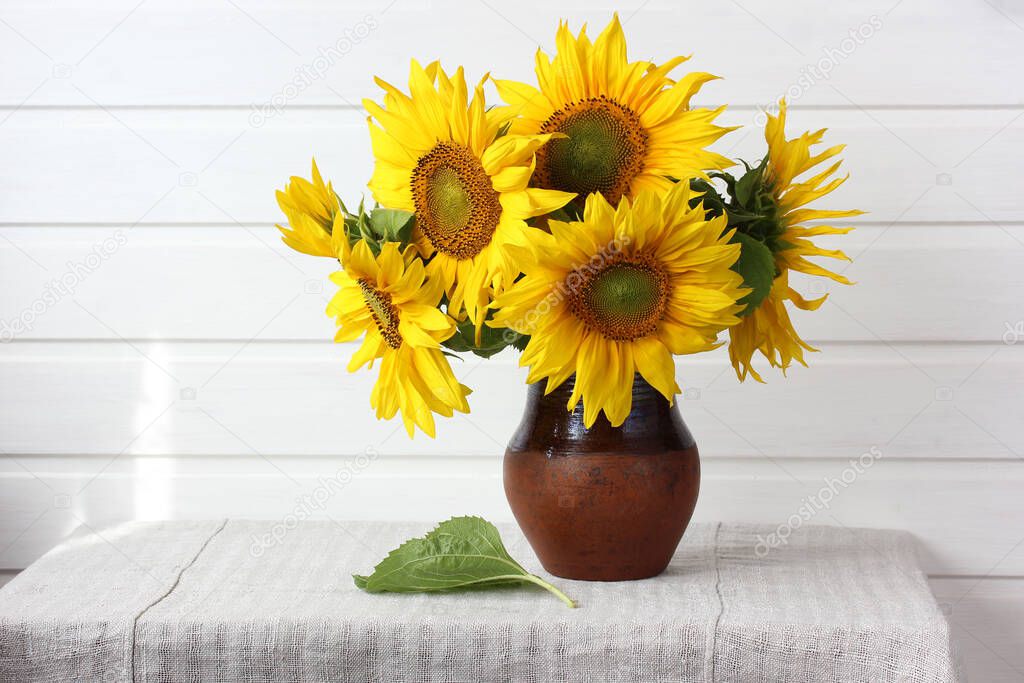 bouquet of sunflowers in a rustic clay jug on the table on a light background. garden flowers, summer still life.
