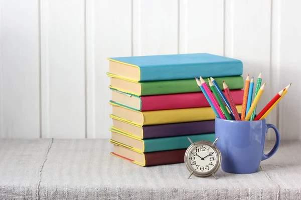本や色鉛筆や目覚まし時計がテーブルの上に置かれています 学校に戻り知識の日 カラーカバーの教科書は — ストック写真