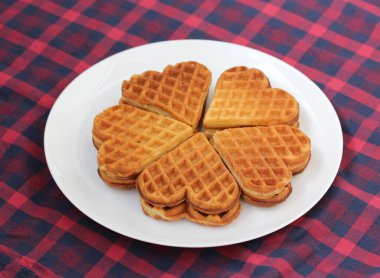 Kırmızı kareli masa örtüsü üzerinde beyaz bir tabakta kalp şeklinde waffle, tatlı..