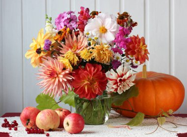 Masada çiçek, elma ve balkabağı demeti varken sonbahar ışığı hayat doludur. hasat, bolluk.