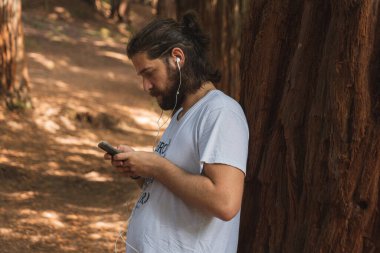 Ormanın ortasında telefona bakan genç adam.