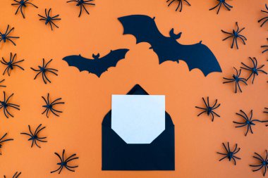 Turuncu arka planda yarasalar ve örümceklerle çevrili beyaz kağıtlı siyah bir zarf.