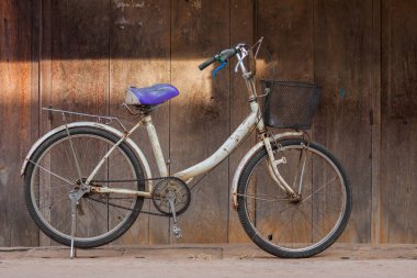 Tayland 'ın kuzeydoğusunda bulunan eski evin ahşap desenli duvarının önünde eski beyaz bisiklet parkı.