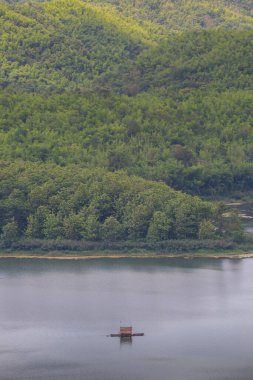 Tayland 'ın kuzeydoğusunda, bulutlu gökyüzünün altında, yeşil dağın arkasında, su üzerinde yüzen bir sal.