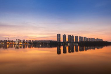 Bir apartman dairesi, gün batımında renkli gökyüzünün altındaki suyun yansımasıdır. Arina Bangkok Tayland 'a çarpma zamanı.