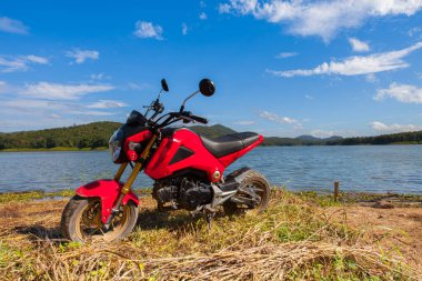Kırmızı motosiklet temiz gökyüzünün altında nehir ve dağ zeminiyle