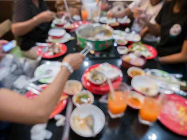 Bir restoranın masasında çeşit çeşit yemek yiyen insanların bulanık görüntüsü.