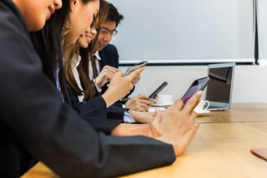 Asyalı iş adamları toplantı odasında, belge ve bilgisayarla ahşap masa üzerine grup tartışması yapıyorlar.