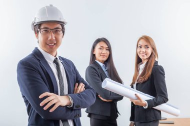 Genç iş adamı siyah takım elbiseli ve beyaz kasklı genç iş kadınının arka planında duruyor.