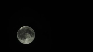 Gece vakti karanlık gökyüzünde hızla hareket eden bir ay bulutlu bir bulutun yanından geçer.
