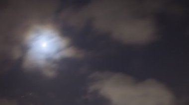 Gece vakti karanlık gökyüzünde hızla hareket eden bir ay bulutlu bir bulutun yanından geçer.