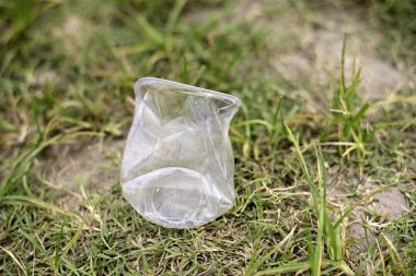Yeşil çim alanında atılmış plastik su bardağı.