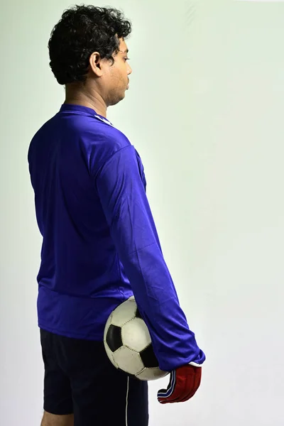 Soccer goalkeeper standing with soccer ball to play against grey background.