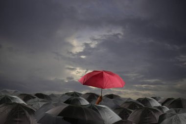 Bulutlu bir günde birçok siyah şemsiye arasında kırmızı şemsiye