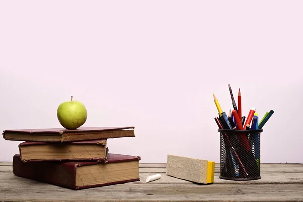 Green apple on book with pen stand isolated on wooden table against white.