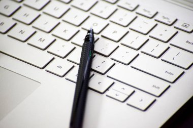 Dizüstü bilgisayarın üzerine uzanmış bir kalemin yakın plan görüntüsü.