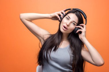Dinleme müzik setinden, ellerini başında, turuncu arka plana karşı bir güzel kız portresi. Yaşam tarzı, insan ve teknoloji kavramı