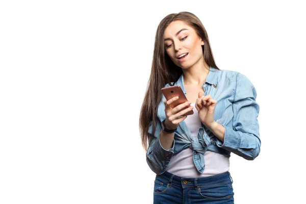 Porträt einer jungen brünetten Frau, die mit überraschtem Gesichtsausdruck vor weißem Hintergrund isoliert auf das Smartphone blickt. Lebensstil, Menschen und Technologiekonzept — Stockfoto