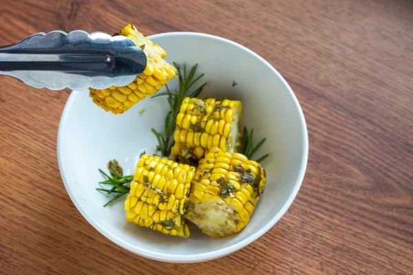 Cocinado en el horno de maíz con hierbas sobre un fondo de madera en un tazón blanco, cocinar mazorcas de maíz a mano de chef, vista superior — Foto de Stock
