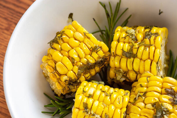Cooked in the oven corn with herbs on a wooden background in white bowl closeup, top view
