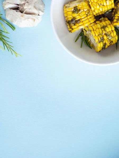 Ψημένα στο φούρνο καλαμπόκι με βότανα σε λευκό μπολ, σκόρδο και δεντρολίβανο επίπεδη Απλώστε μπλε φόντο, το top view, αντιγράψτε το χώρο για το κείμενο — Φωτογραφία Αρχείου