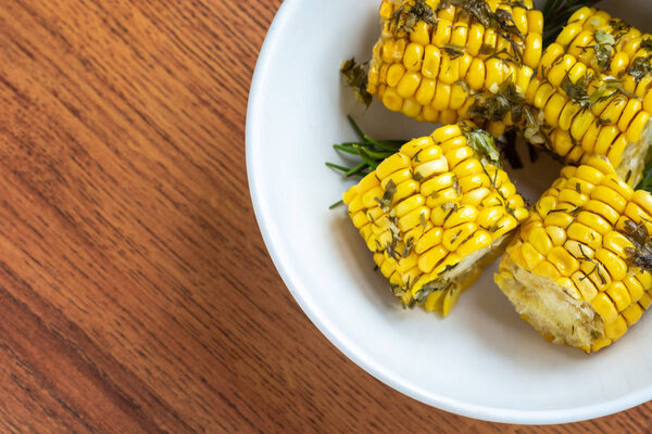 Cooked in the oven corn with herbs on a wooden background in white bowl closeup, top view, copy space for text