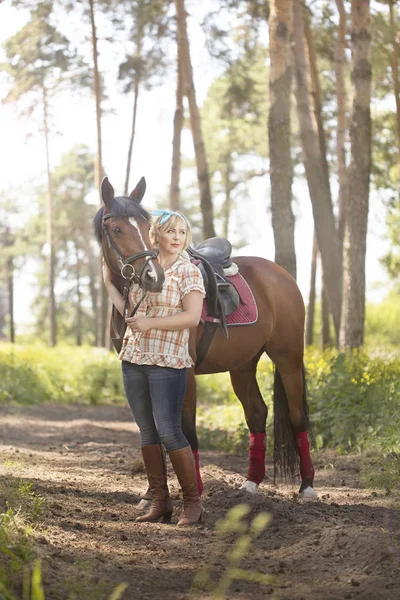 Neşeli, güzel sarışın kız bir ormandaki yaz güneşli havalarda nehrin bir atı ile yürüyor