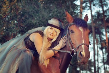 güzel kız sarışın binici at yürüyüş iğne yapraklı orman elbiseli şapkalı