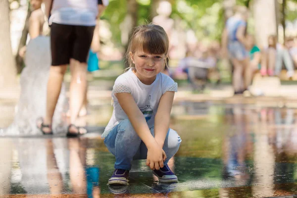 Güzel gülümseyen yaramaz ışık saçlı kız çeşmenin bir güneşli yaz parkta yürüyen bir T-shirt giyen kot pantolon