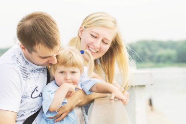 Annem ve babam ile bir küçük sarışın kız güzel bir güneşli yaz yağmur nehir kıyısında bir şehir Parkta oynayan genç çift