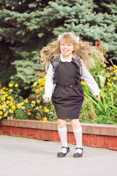 少し陽気な青い瞳の女の子 日に制服で弓と髪の息切れ一流実行学校で浮かれてジャンプ — ストック写真