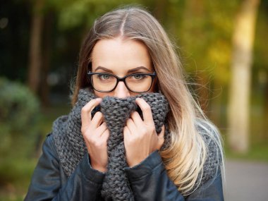 bir güzel şık genç sarışın kız siyah gözlük deri ceket ve örme eşarp makyajlı portresi Don yukarıya sonbahar soğuk parkta gülümsüyor