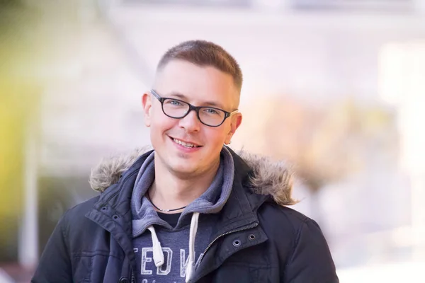 handsome cheerful short-cut man in black glasses in a black jacket walks through the autumn streets of the city