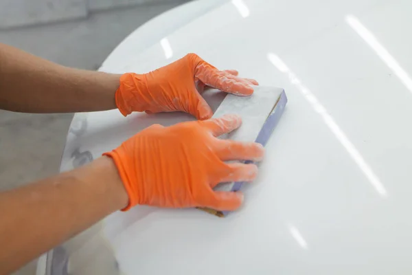 men\'s hands in orange gloves take the form of the hood for the subsequent eipoking of the car. man working in a car garage