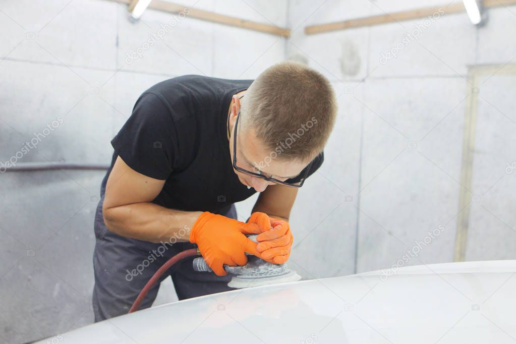 cute cheerful guy with glasses polishes the hood of a car pneumatic polishing machine
