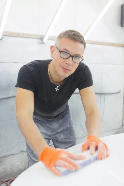 cute guy in black glasses with orange gloves displays the shape of the hood for the subsequent painting of the car. guy - a house painter working on a car in the garage